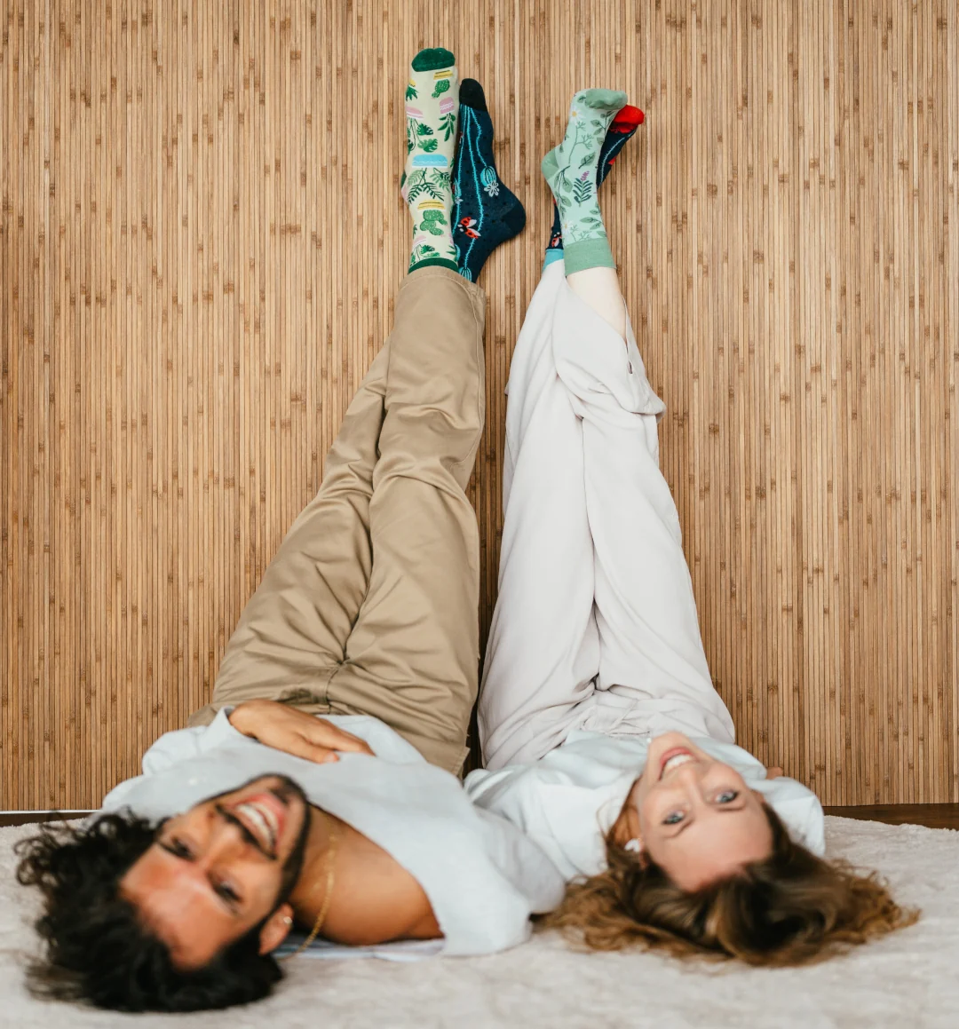 Ursula und Stamatis liegen auf dem Boden, die Beine mit bunten Socken an der Wand